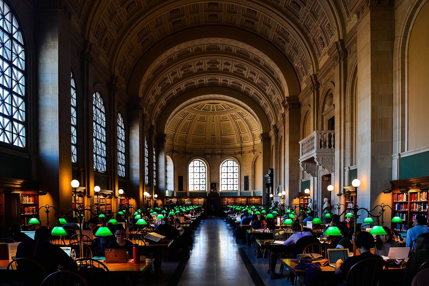 The barrel-vaulted Bates Hall reading room at the Boston Public Library, lined with long oak tables and green lamps.