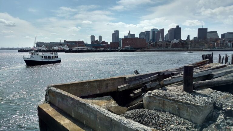 An MBTA harbor ferry crossing Boston Harbor with the downtown skyline behind it.