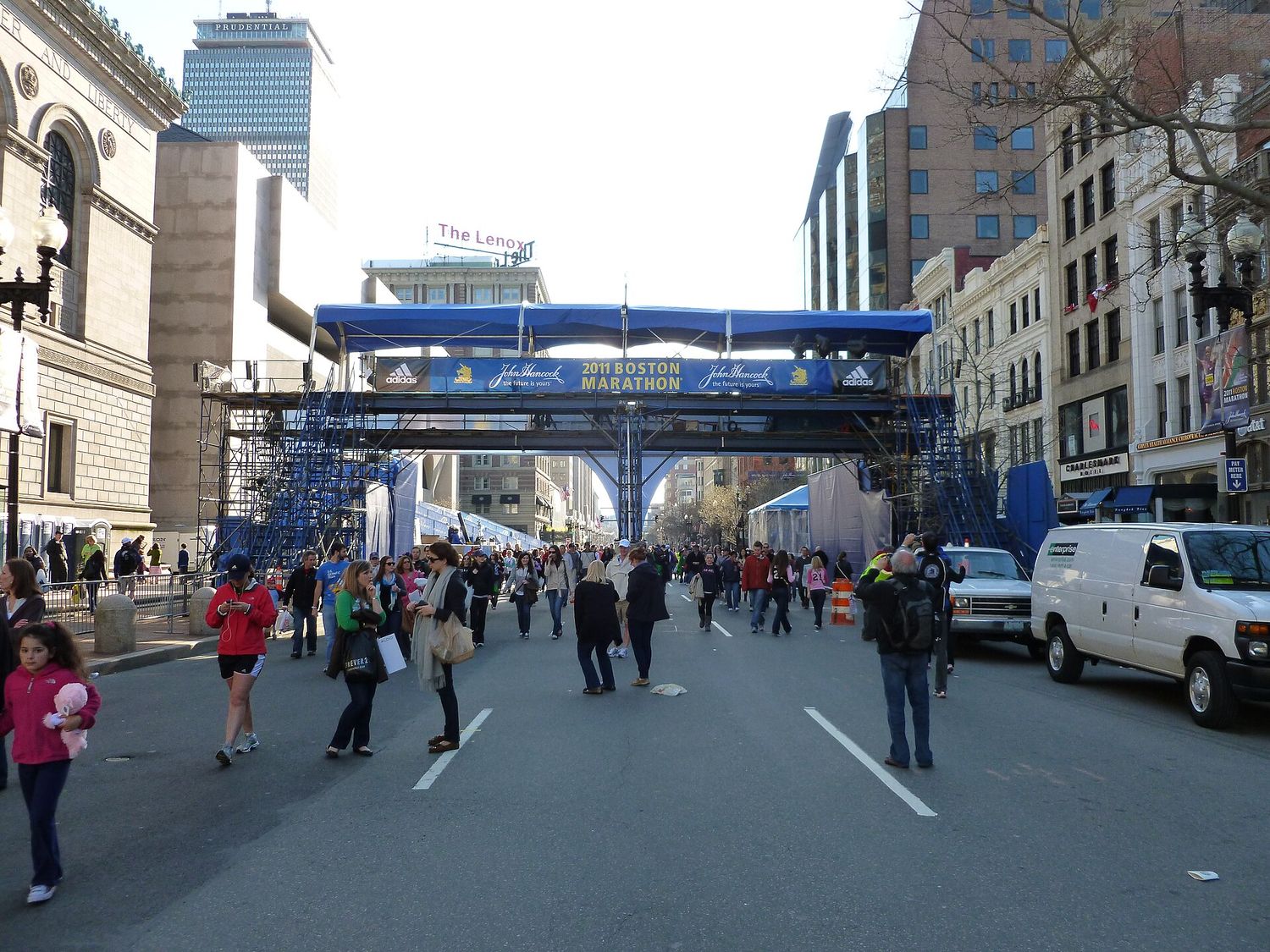 The Boston Marathon finish line gantry set up across Boylston Street, with crowds walking beneath it and the Prudential Tower behind.