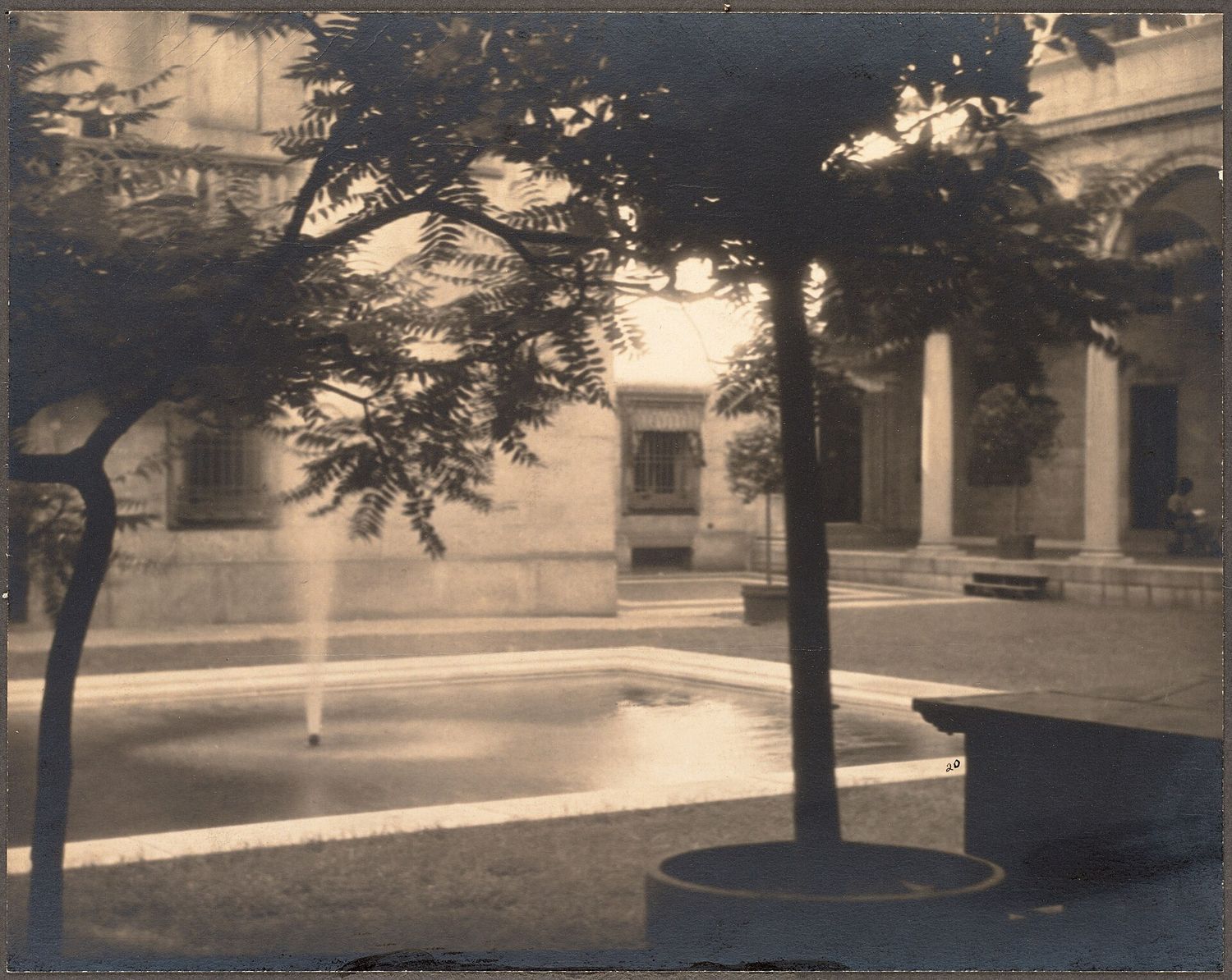 An early twentieth-century sepia photograph of the Boston Public Library courtyard, with a rectangular pool and a single jet of water, trees in round planters and an arcade of columns behind.
