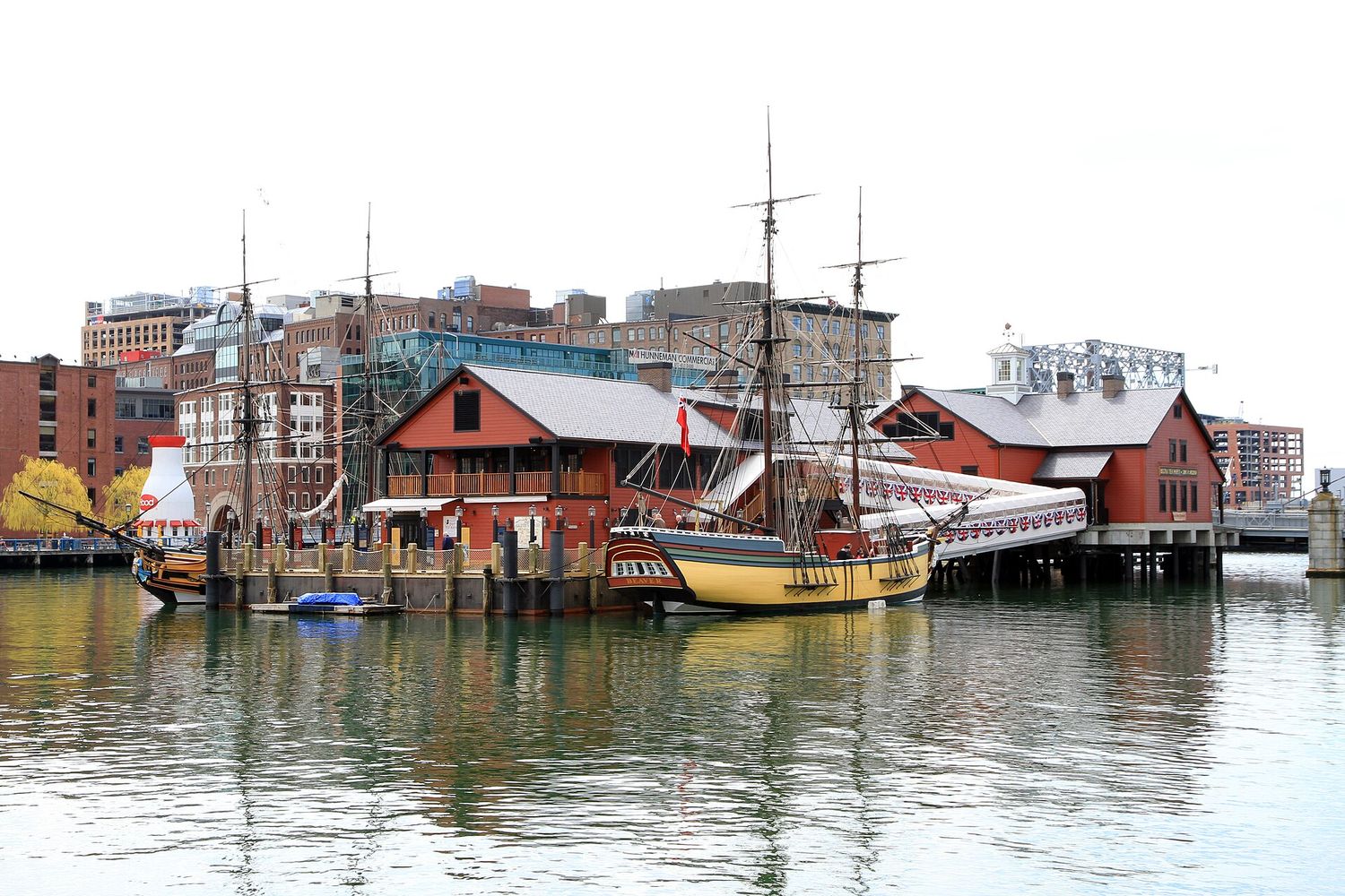 Two replica eighteenth-century sailing ships moored beside the red wooden buildings of the Boston Tea Party Ships and Museum on Fort Point Channel.