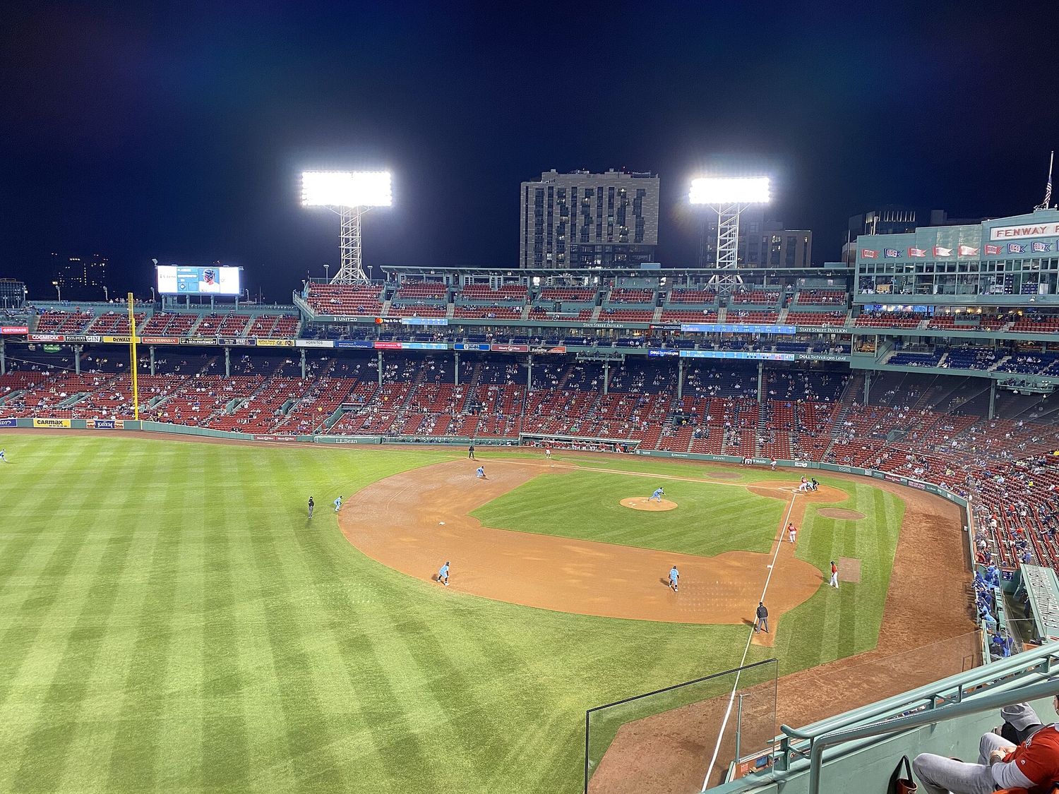 A night game at Fenway Park seen from high above left field, with the infield lit and the grandstand behind.