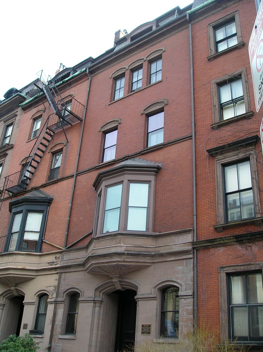 The brick and brownstone facade of the Gibson House Museum on Beacon Street in Back Bay, with a bay window above an arched entrance and a small bronze plaque beside the door.