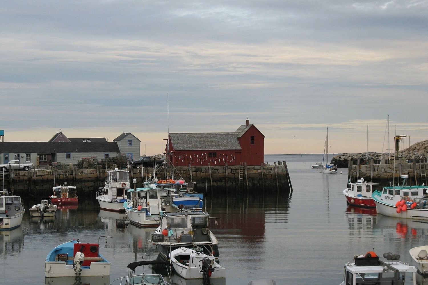 Motif No. 1, a red fishing shack on Bradley Wharf in Rockport, Massachusetts, with lobster boats moored in the harbor.