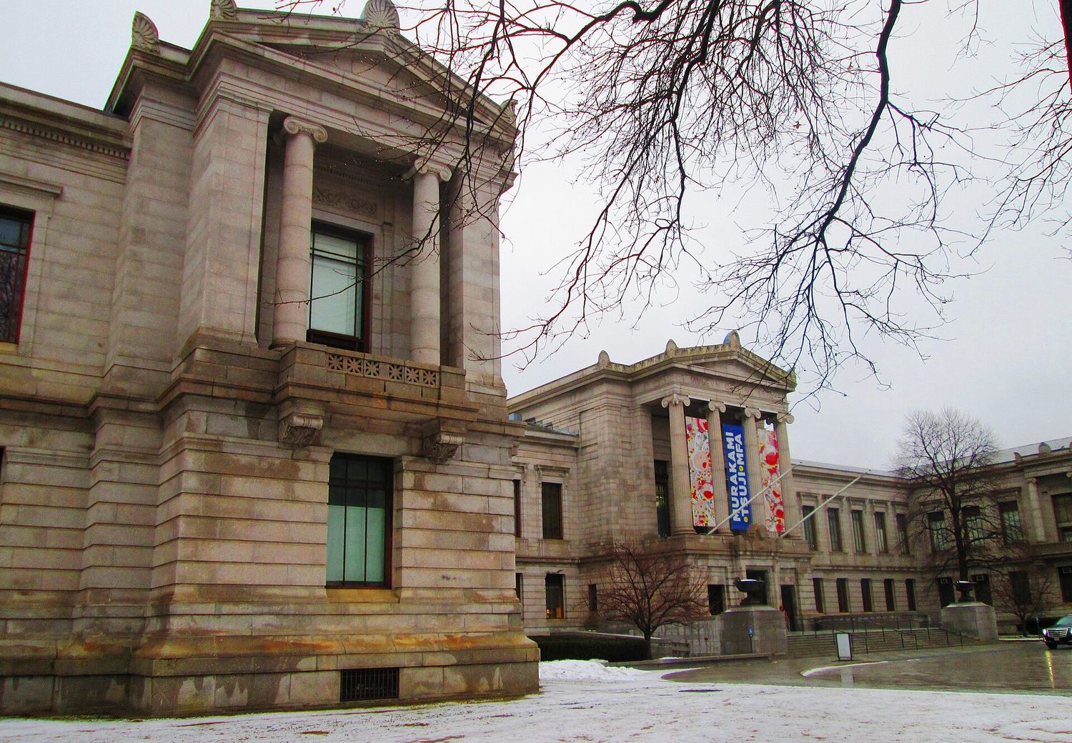 The granite Huntington Avenue facade of the Museum of Fine Arts, Boston, with Ionic columns and a banner hanging between them on a gray winter day.
