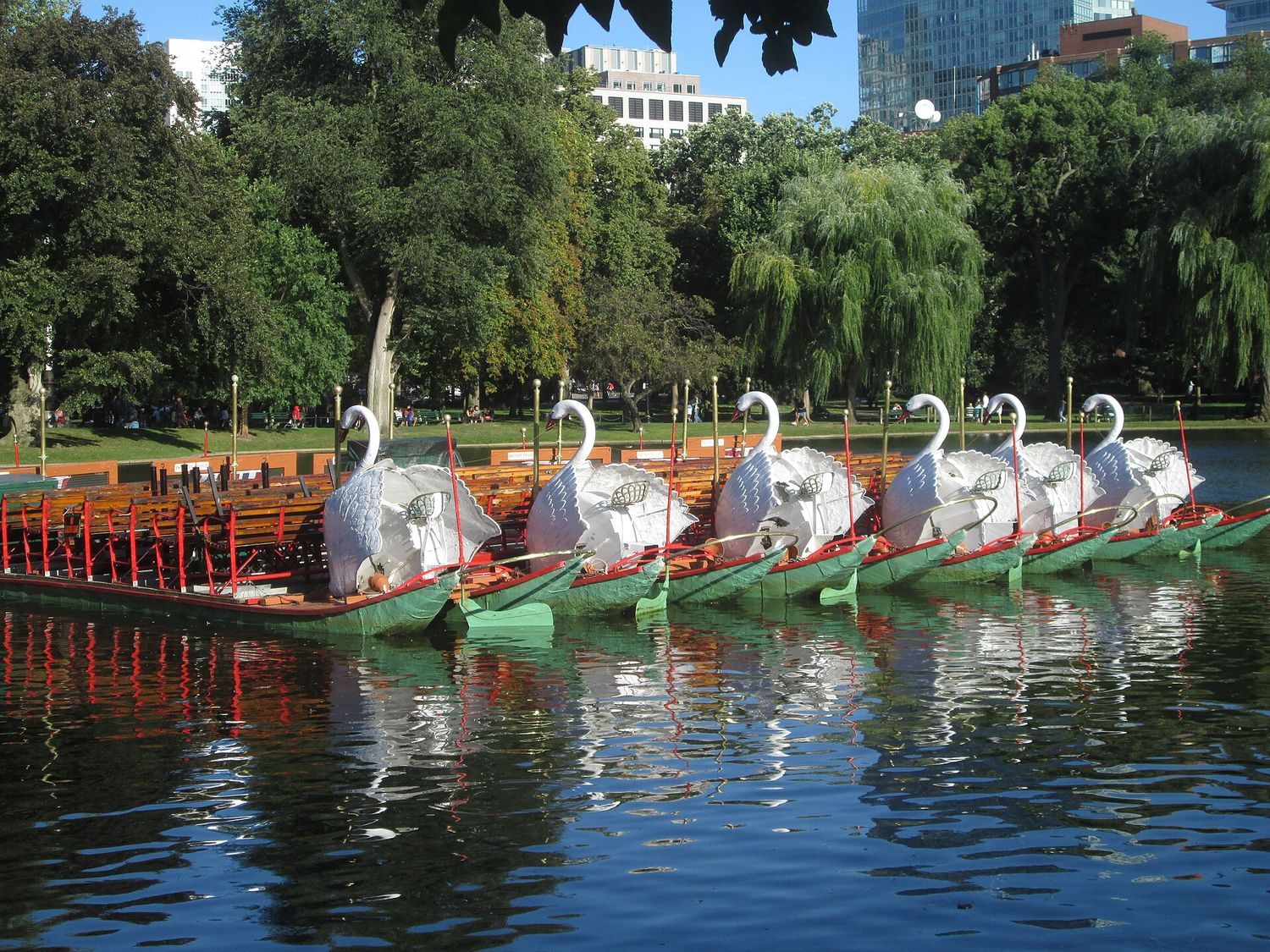 Two pedal-powered Swan Boats moored on the lagoon in Boston Public Garden, framed by willows.